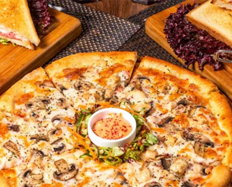 Pizza with mushrooms and herbs, a dipping sauce cup at the center on a wooden table.